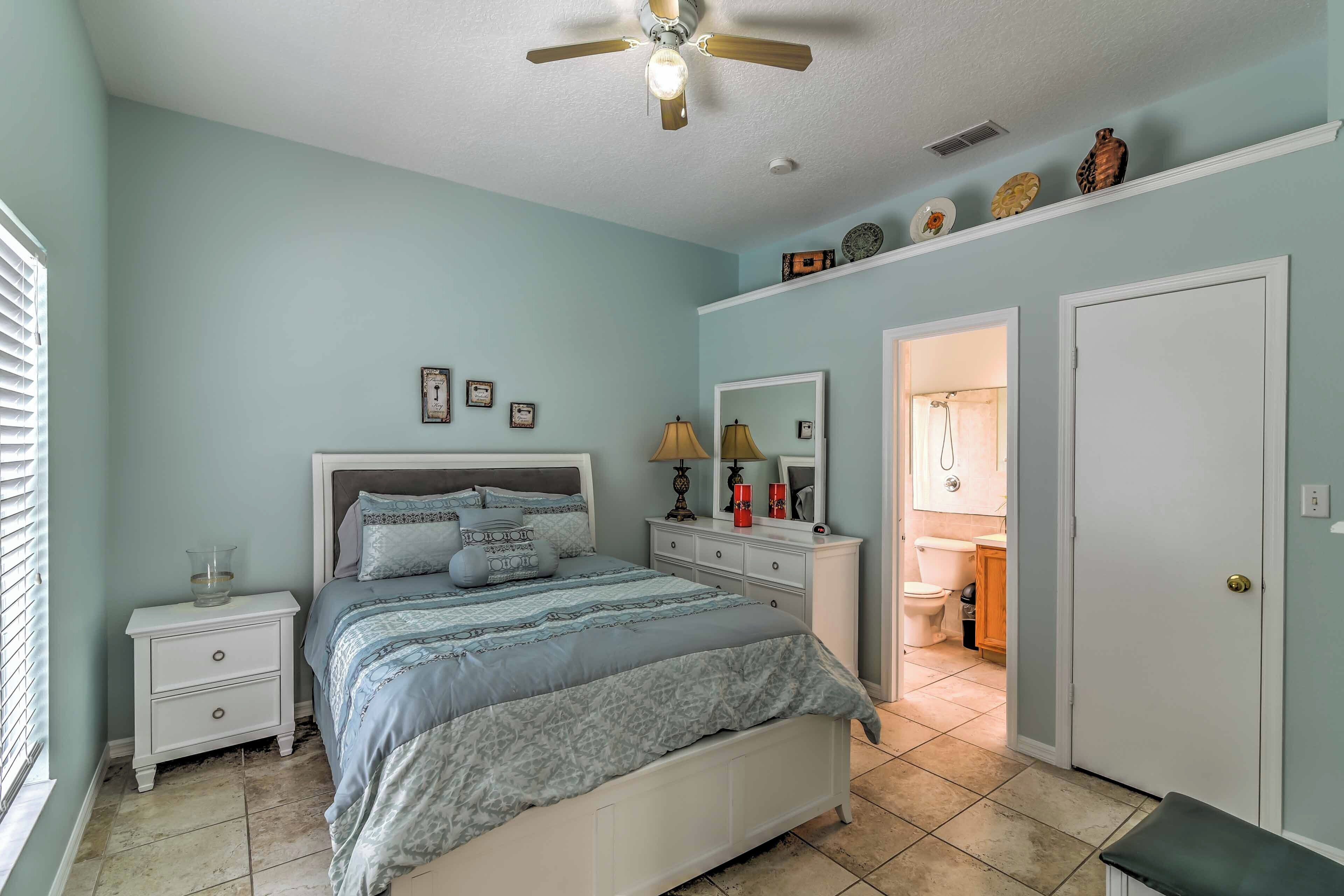 A bedroom with a bed, nightstands, a dresser, a ceiling fan, and a bathroom visible through an open door.