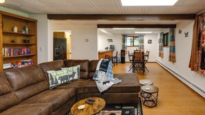 A living room with a brown leather couch, a wooden coffee table, and a bookshelf filled with books. - Ideally Located Fairbanks Vacation Rental! (Fairbanks)