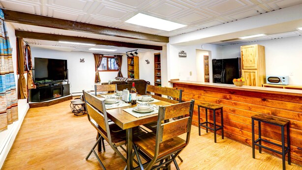 A dining area with a wooden table set for four, surrounded by metal chairs. A kitchen with a wooden countertop and a refrigerator is visible in the background. - Ideally Located Fairbanks Vacation Rental! (Fairbanks)