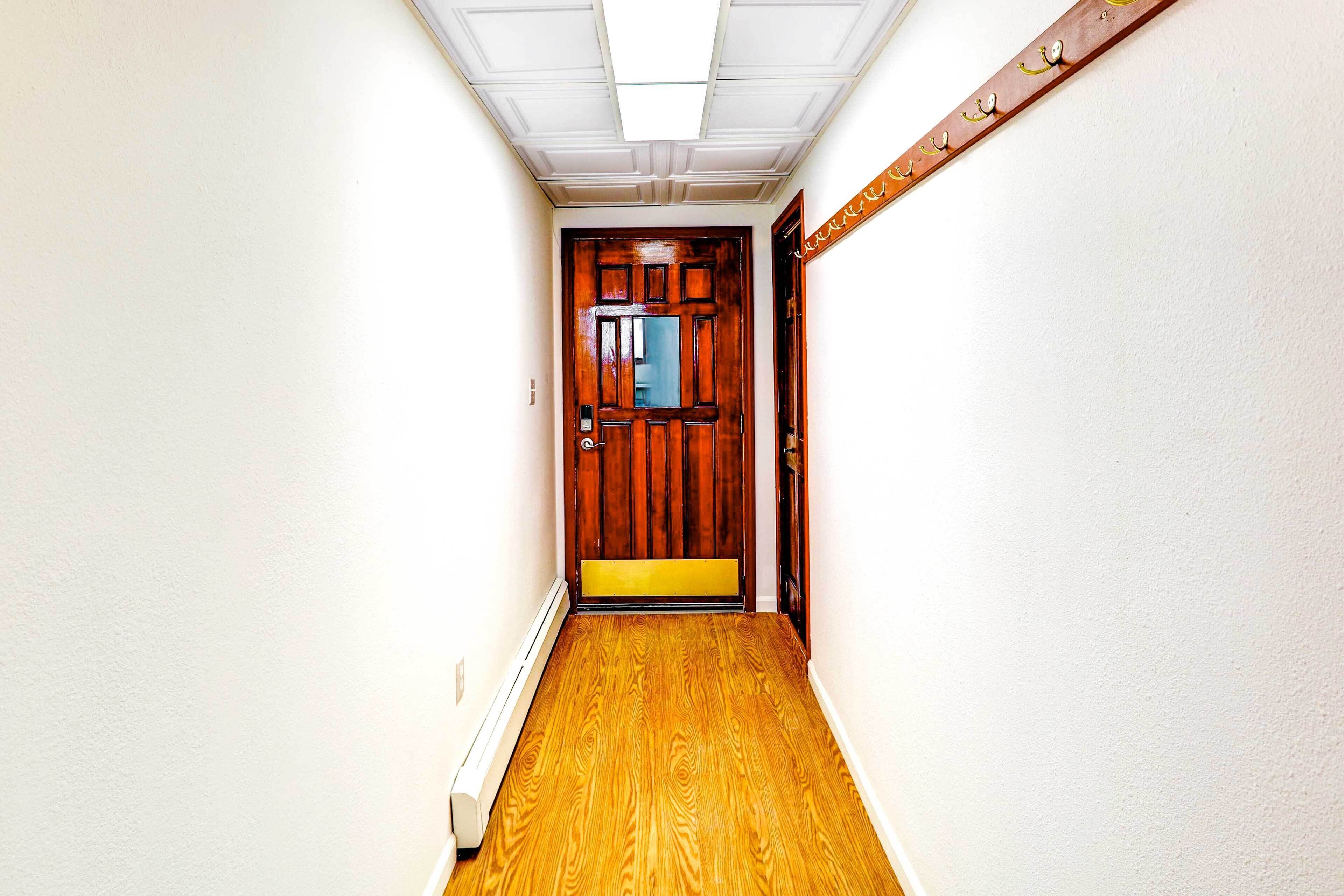 A narrow hallway with a wooden door at the end, white walls, and a wooden floor.