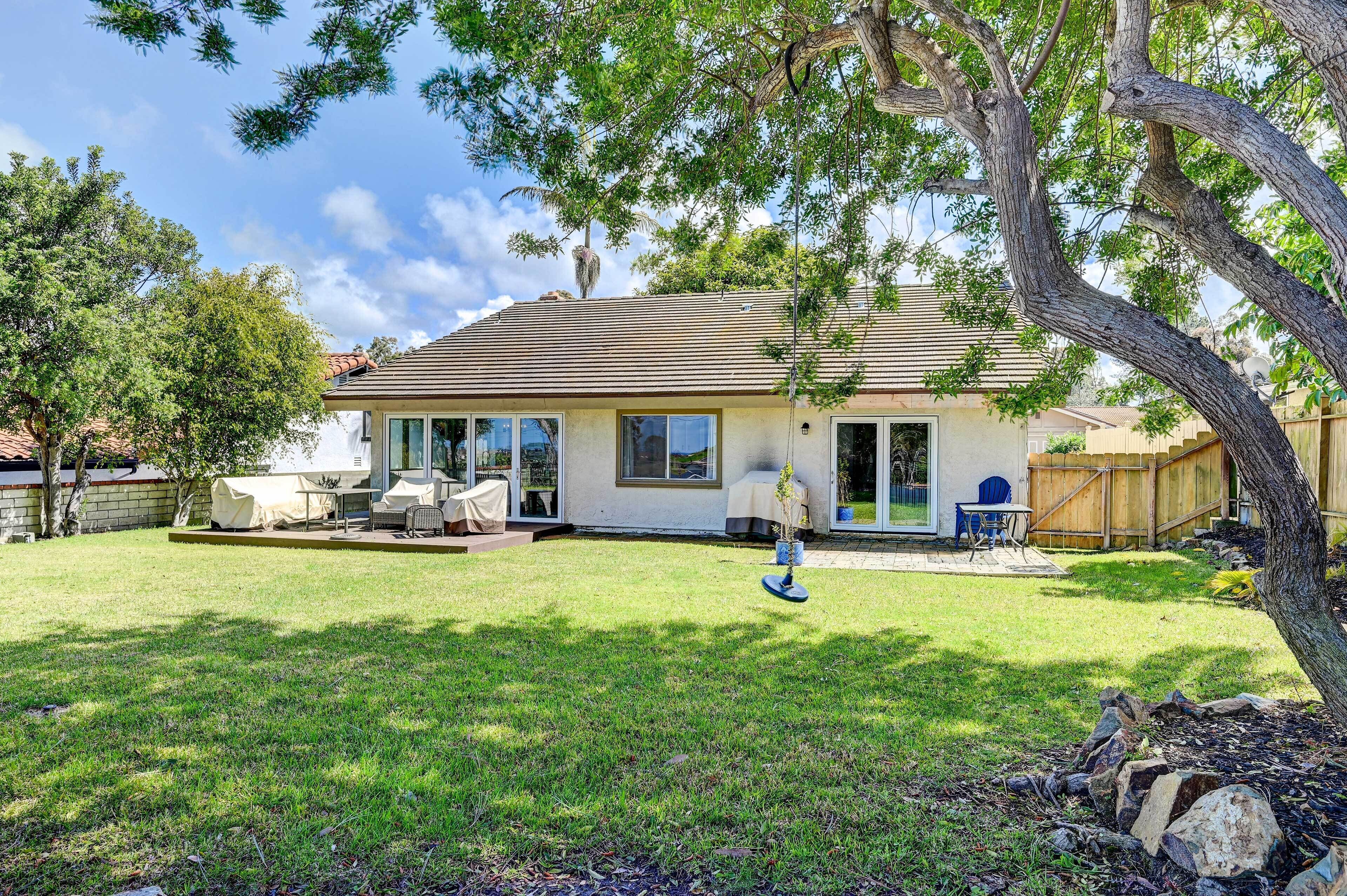 A house with a covered patio, a lawn, and a tree.