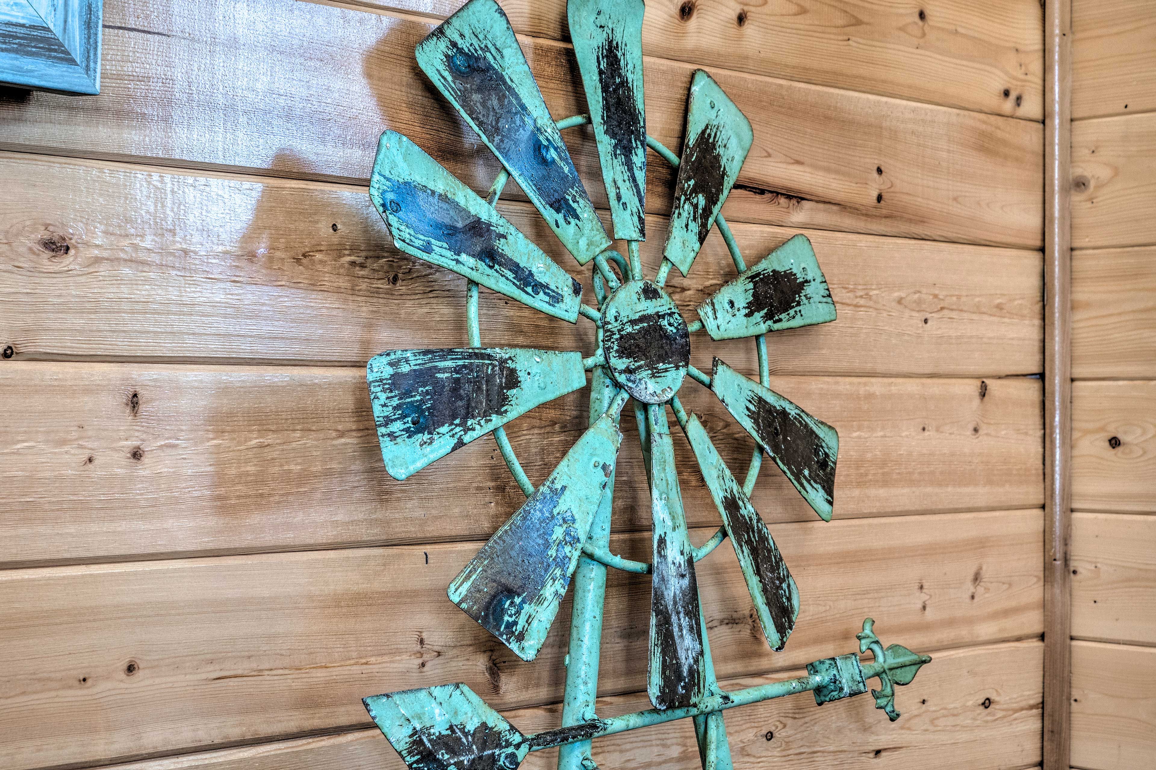A rustic windmill with a weathered, teal-colored metal finish mounted on a wooden wall.