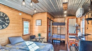 A cozy cabin with a large bed, a small dining table, a kitchenette, and a bunk bed. - Sunny 'catfish Cabin' w/ Views of Toledo Bend (Many)