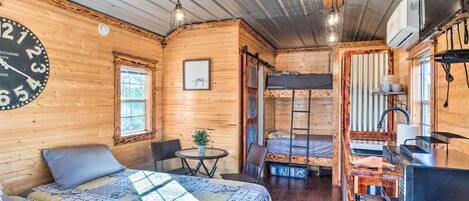A cozy cabin with a large bed, a small dining table, a kitchenette, and a bunk bed.