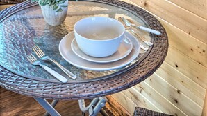 A glass table with a white bowl and cutlery, a potted plant, and a wicker chair. - Sunny 'catfish Cabin' w/ Views of Toledo Bend (Many)