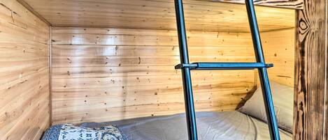 Una habitación de cabaña de madera con una litera, una escalera y una colcha estampada.