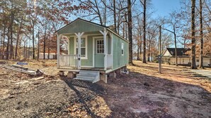 A small, single-story cabin with a porch, situated in a wooded area with a dirt ground. - Sunny 'catfish Cabin' w/ Views of Toledo Bend (Many)