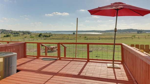 A wooden deck with a red umbrella, overlooking a grassy field and a body of water. - Private Deck & Water View, Walk to Canyon Lake (Canyon Lake)