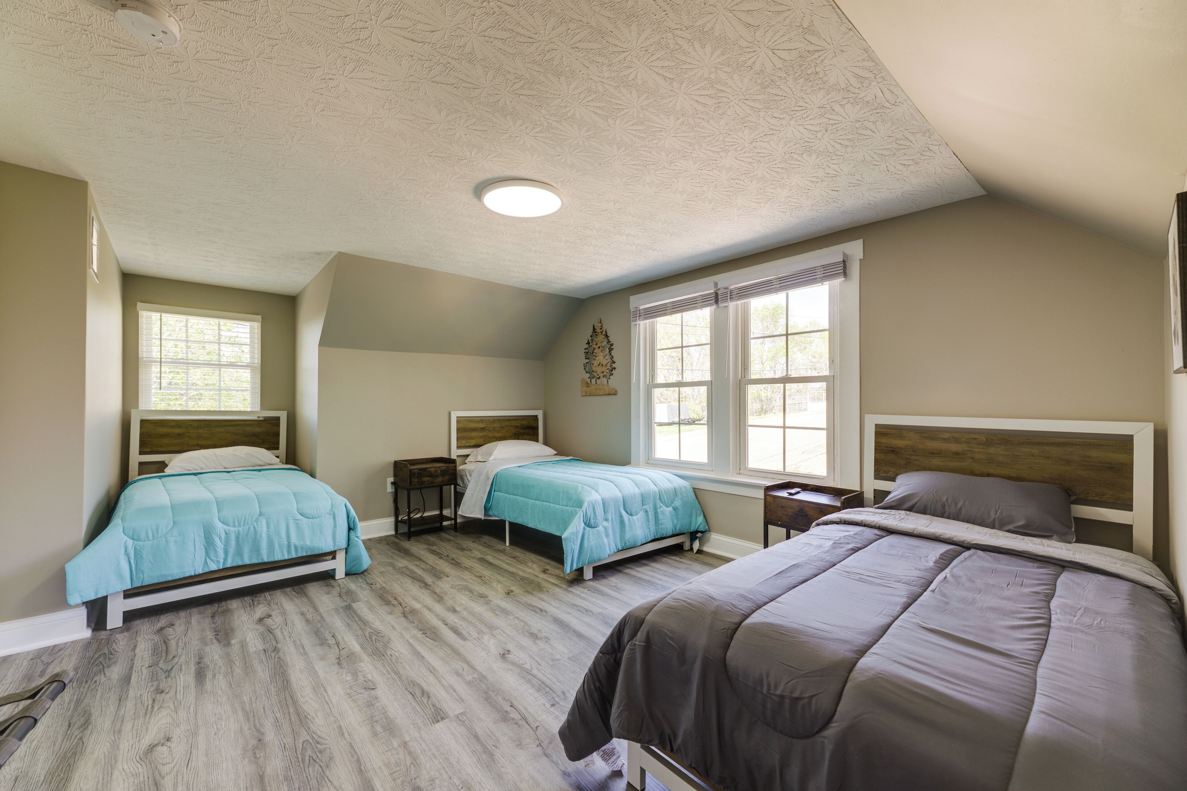 Une chambre avec deux lits, un plancher en bois et un plafond orné d’un motif texturé.