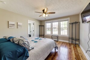 Une chambre à coucher avec un lit, un ventilateur de plafond, une fenêtre et un téléviseur fixé au mur.