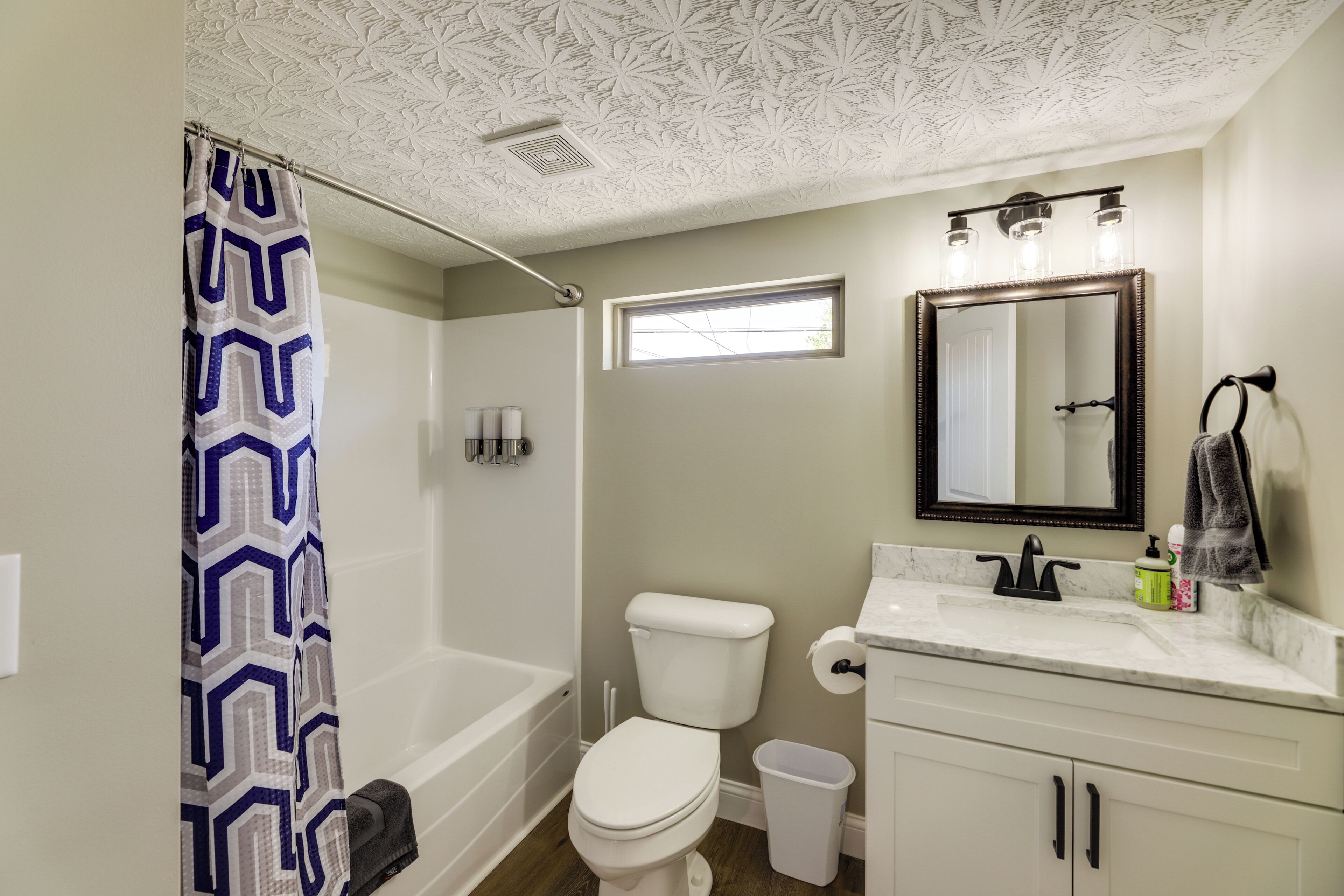 Une salle de bain avec un rideau de douche, des toilettes, un lavabo, un miroir et une fenêtre.