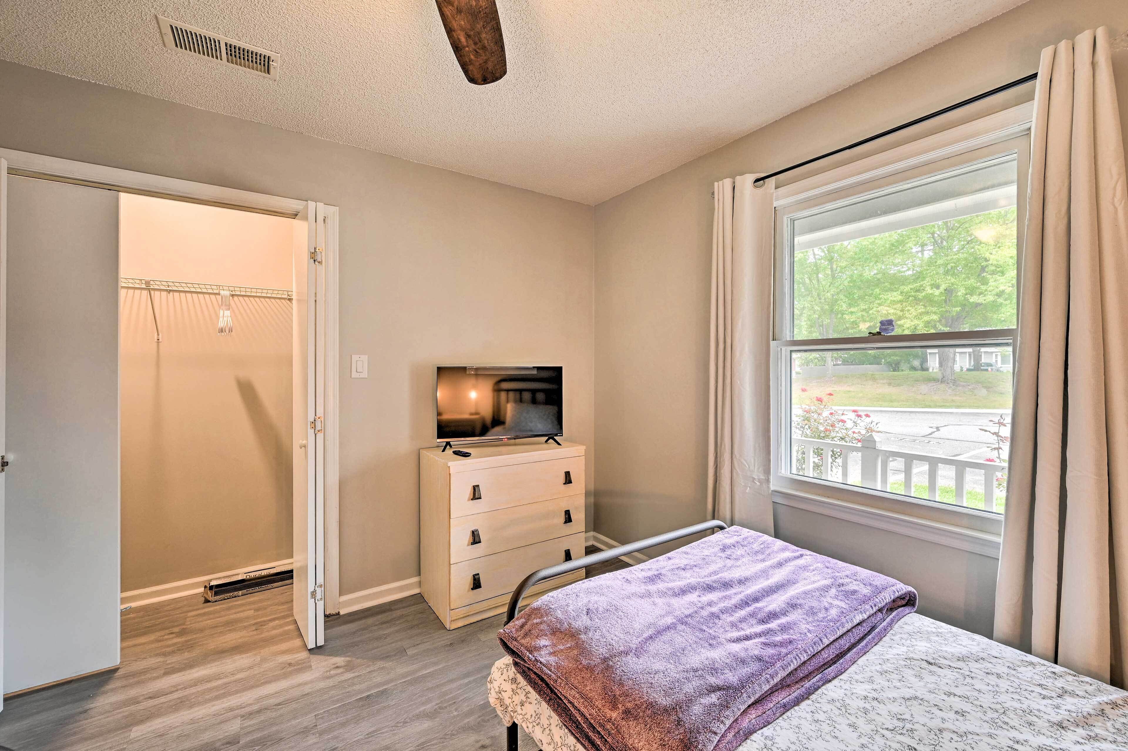 A bedroom with a bed, a dresser, a ceiling fan, a window with curtains, and a view of the outside.