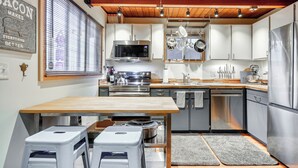 Une cuisine moderne dotée d’appareils électroménagers en acier inoxydable, d’un plafond en bois et d’une fenêtre avec des stores.