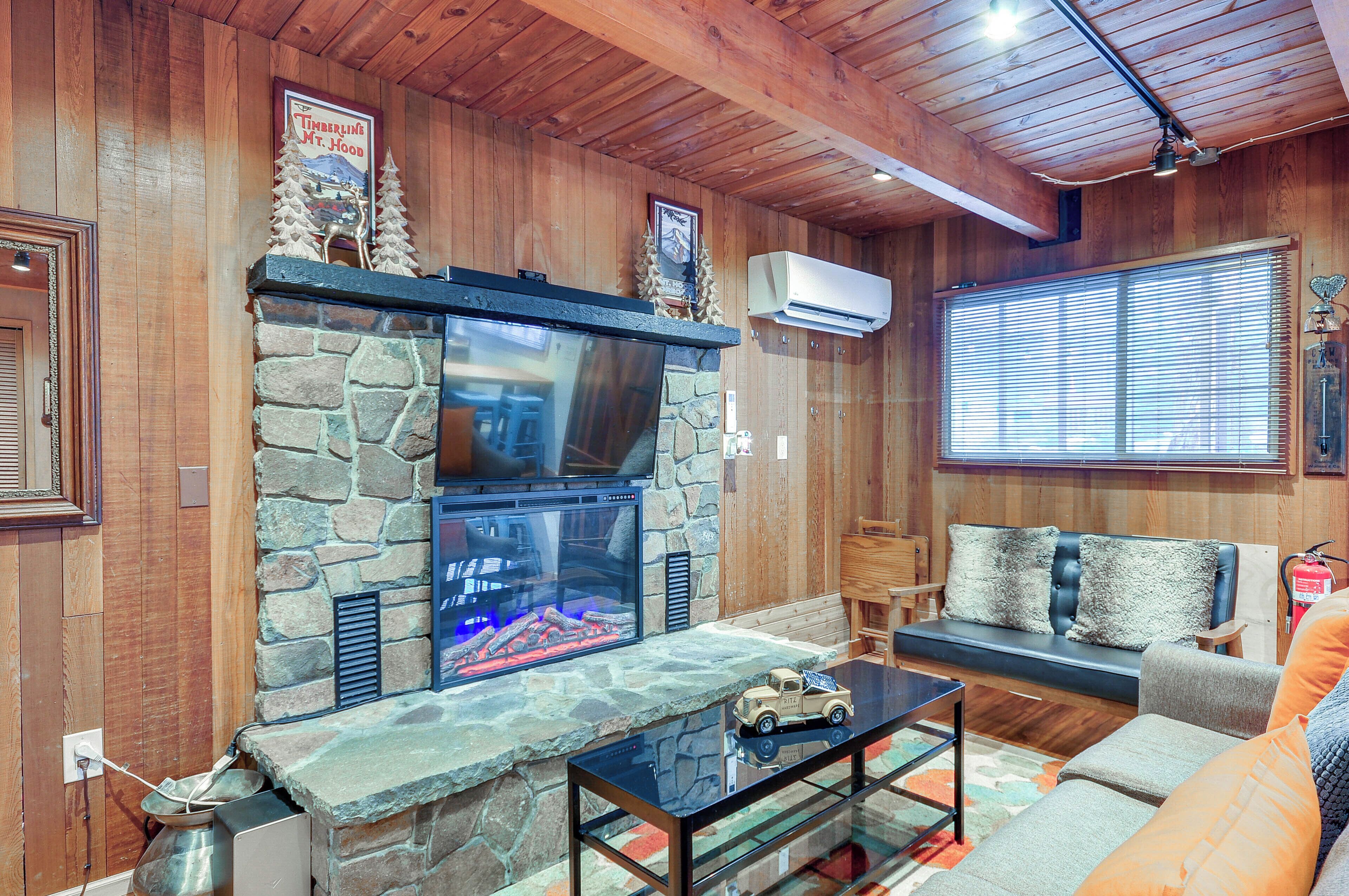 A cozy living room with a stone fireplace, wooden walls, a comfortable sofa, and a television.