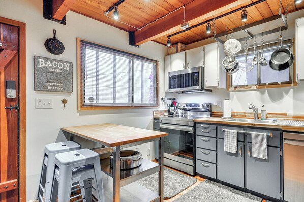 A modern kitchen with a wooden ceiling, stainless steel appliances, and a window with blinds.