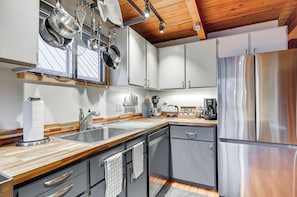A modern kitchen with stainless steel appliances, wooden countertops, and a wooden ceiling.