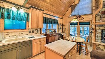A rustic kitchen with wooden cabinets, a large island, and a dining area with wooden chairs.