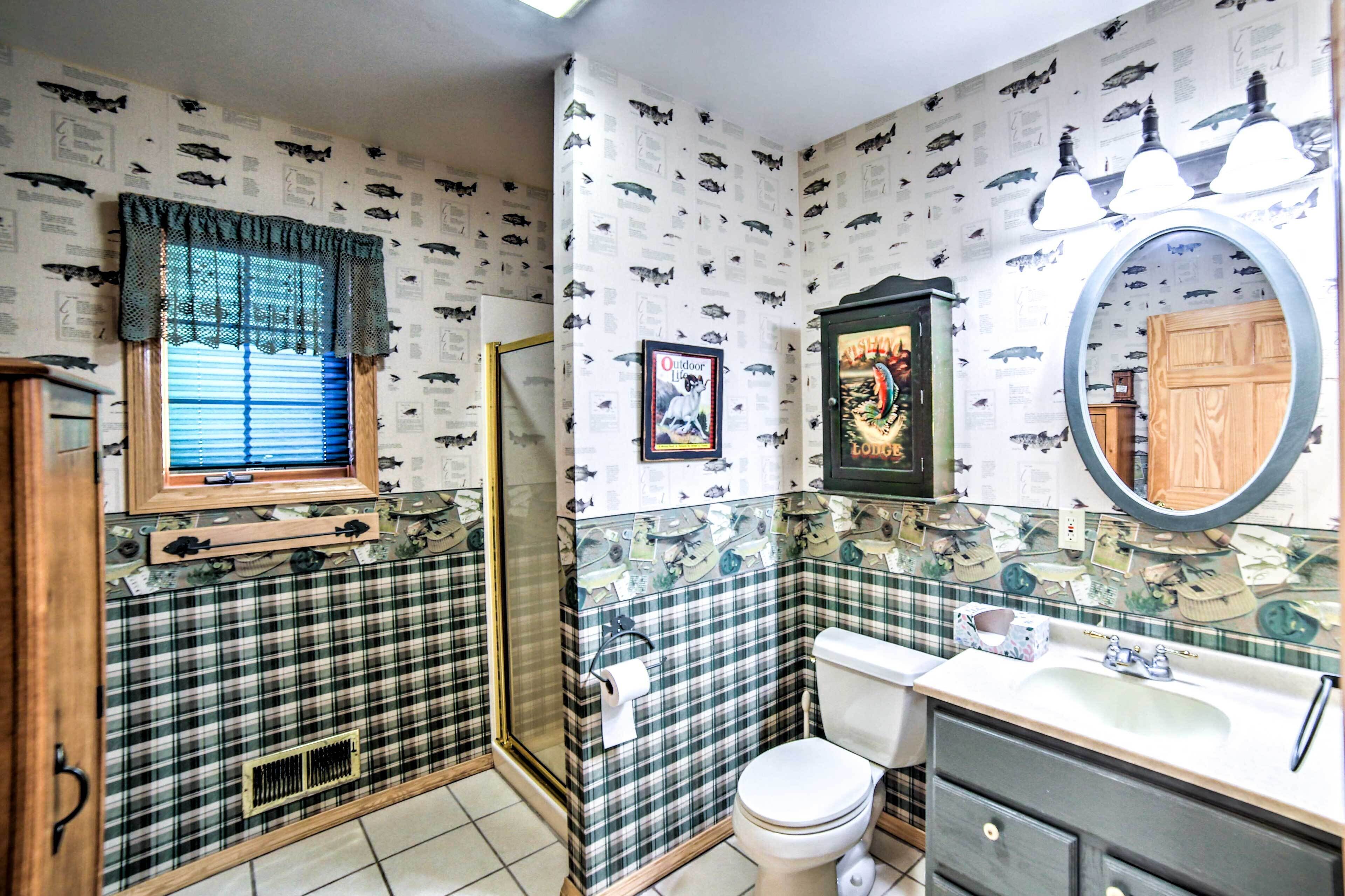 Une salle de bain avec une cabine de douche à motifs écossais, des toilettes, un lavabo avec un miroir et une fenêtre avec des stores.