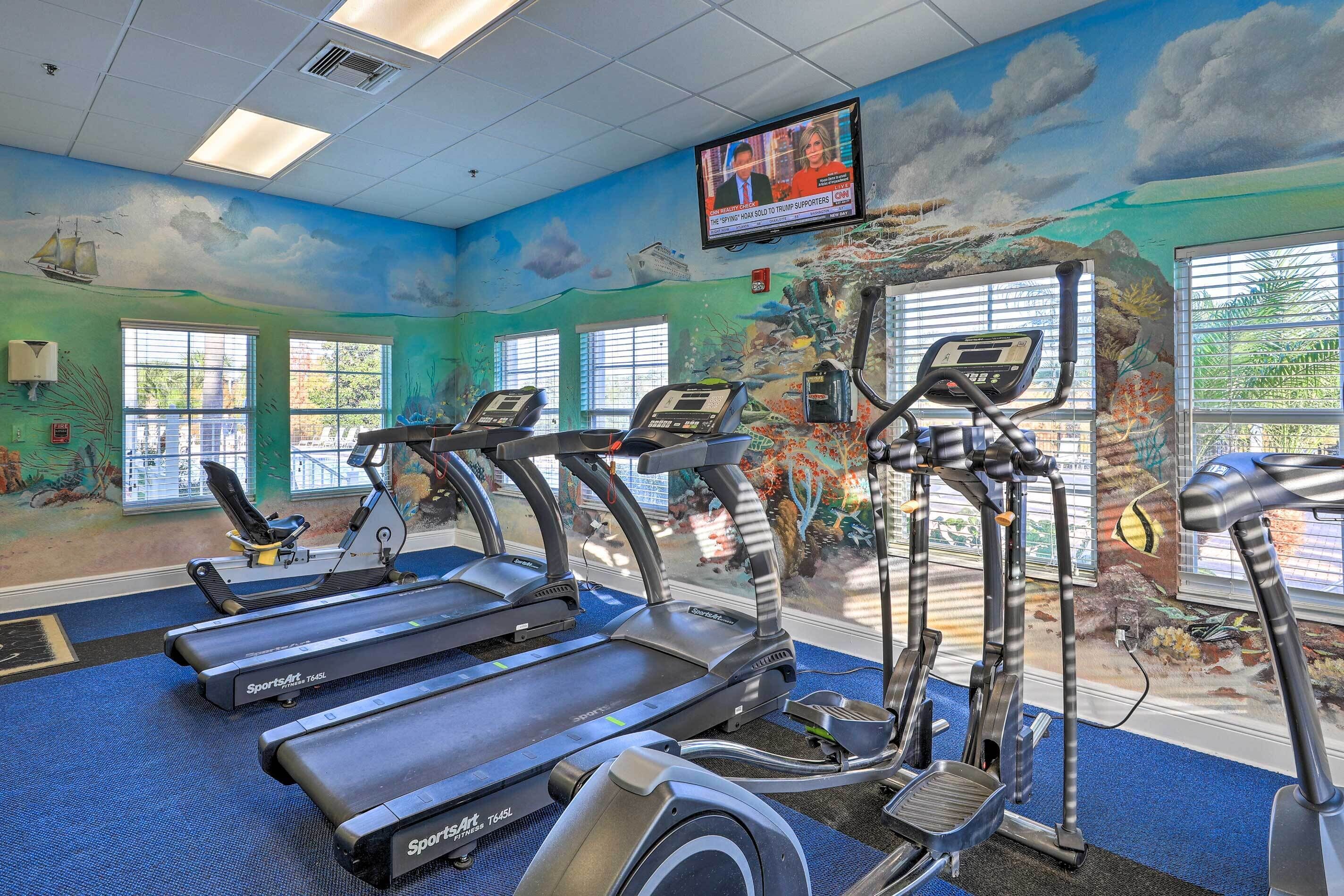 Ein Fitnessstudio mit Laufbändern, Crosstrainern und einem Fernsehbildschirm, der eine Nachrichtensendung zeigt.