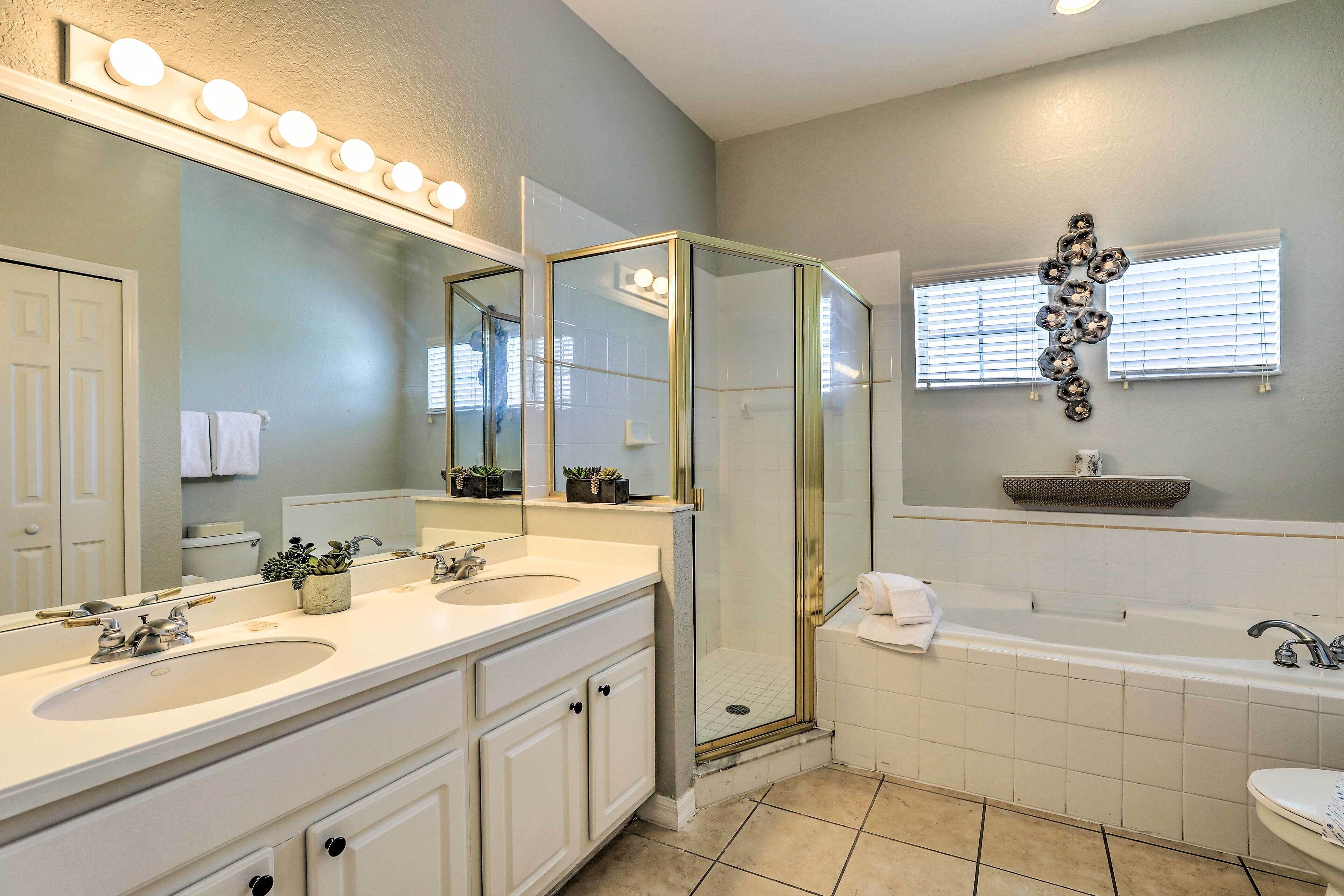 A bathroom with a double sink vanity, a glass shower enclosure, a bathtub, and a large mirror with lights.