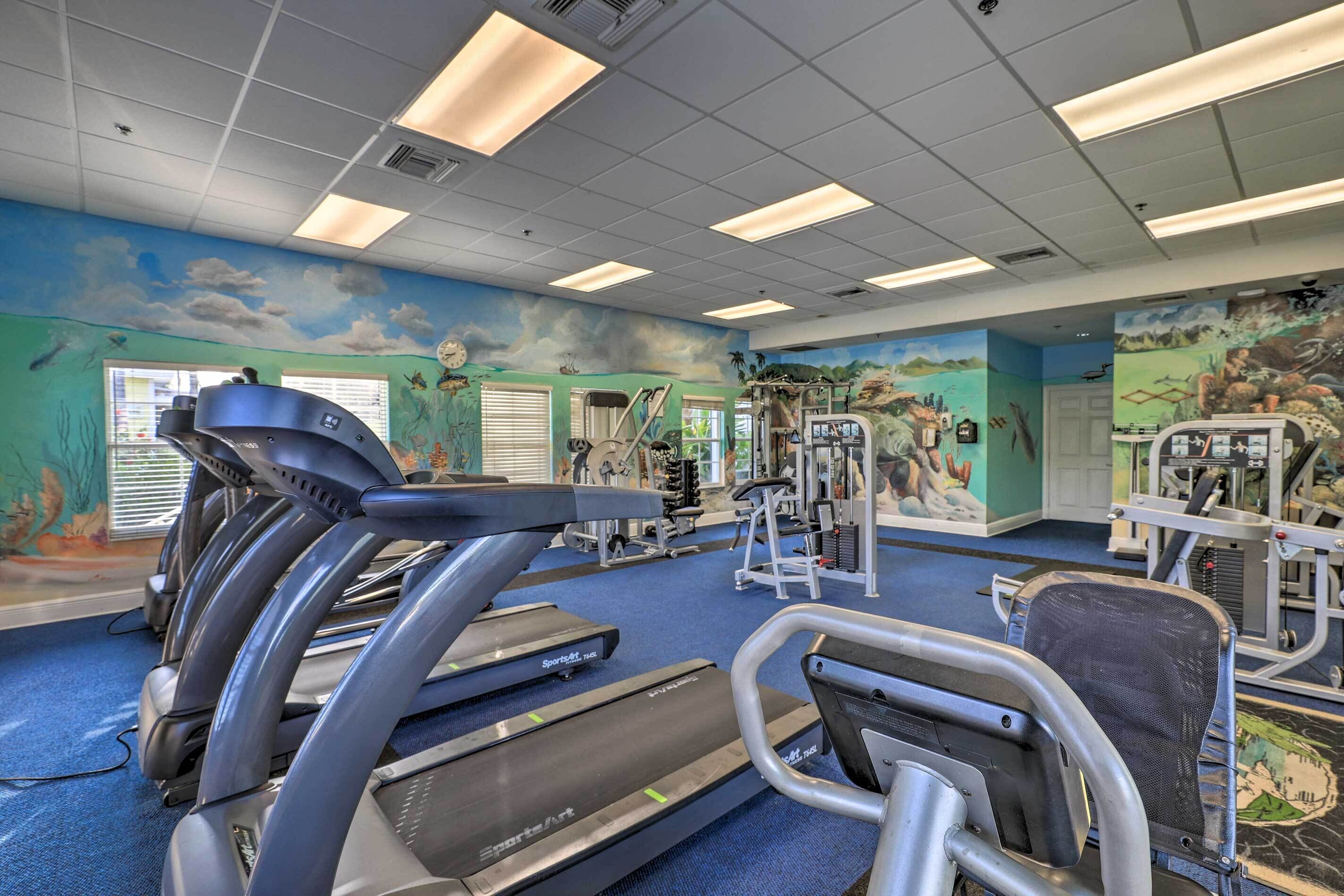 A gym with treadmills, weight machines, and a mural on the wall.