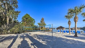 Ein Beachvolleyballfeld mit Netz, Palmen und ein Gebäude mit einem Strohdach im Hintergrund.