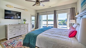 A bedroom with a bed, a ceiling fan, a TV, a dresser, and a window with a view.