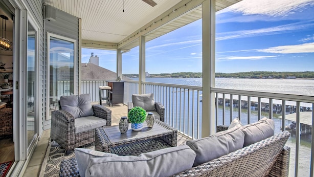 A covered balcony with wicker furniture, a ceiling fan, and a view of a lake.