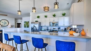 A modern kitchen with a central island, bar stools, stainless steel appliances, and pendant lighting.