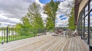 Une terrasse en bois, dotée de mobilier d’extérieur, d’une rambarde et offrant une vue sur des arbres et un bâtiment.