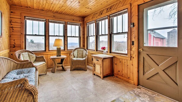 A cozy cabin interior with wooden walls, large windows, wicker furniture, and a door with a cross design. - Wisconsin River Valley Farmhouse: Fire Pit & View (Portage)