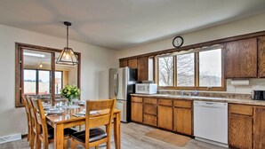 A kitchen with wooden cabinets, a stainless steel refrigerator, a microwave, and a dishwasher. - Wisconsin River Valley Farmhouse: Fire Pit & View (Portage)
