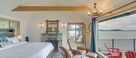A bedroom with a large bed, a fireplace, a ceiling fan, and a view of a lake.