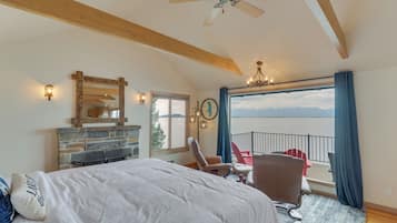 A bedroom with a large bed, a fireplace, a balcony with chairs, and a view of the outdoors.