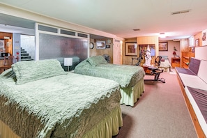 A room with two beds, a desk, a chair, a fan, and a treadmill.