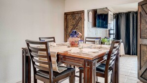 Un coin repas avec une table en bois, dressée pour quatre personnes, entourée de chaises en bois foncé. Un vase décoratif et une petite plante sont posés sur la table.