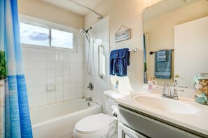 Een badkamer met bad, toilet en wastafel. Er is een raam boven het bad en een welkomstbord aan de muur.