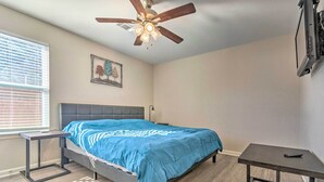 Un dormitorio con cama, ventilador de techo, ventana con persianas y televisor montado en la pared.