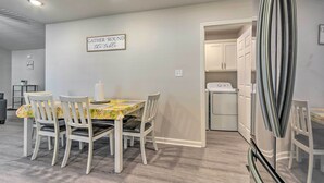 Un comedor con mesa y sillas, una cocina con armarios blancos y un refrigerador.