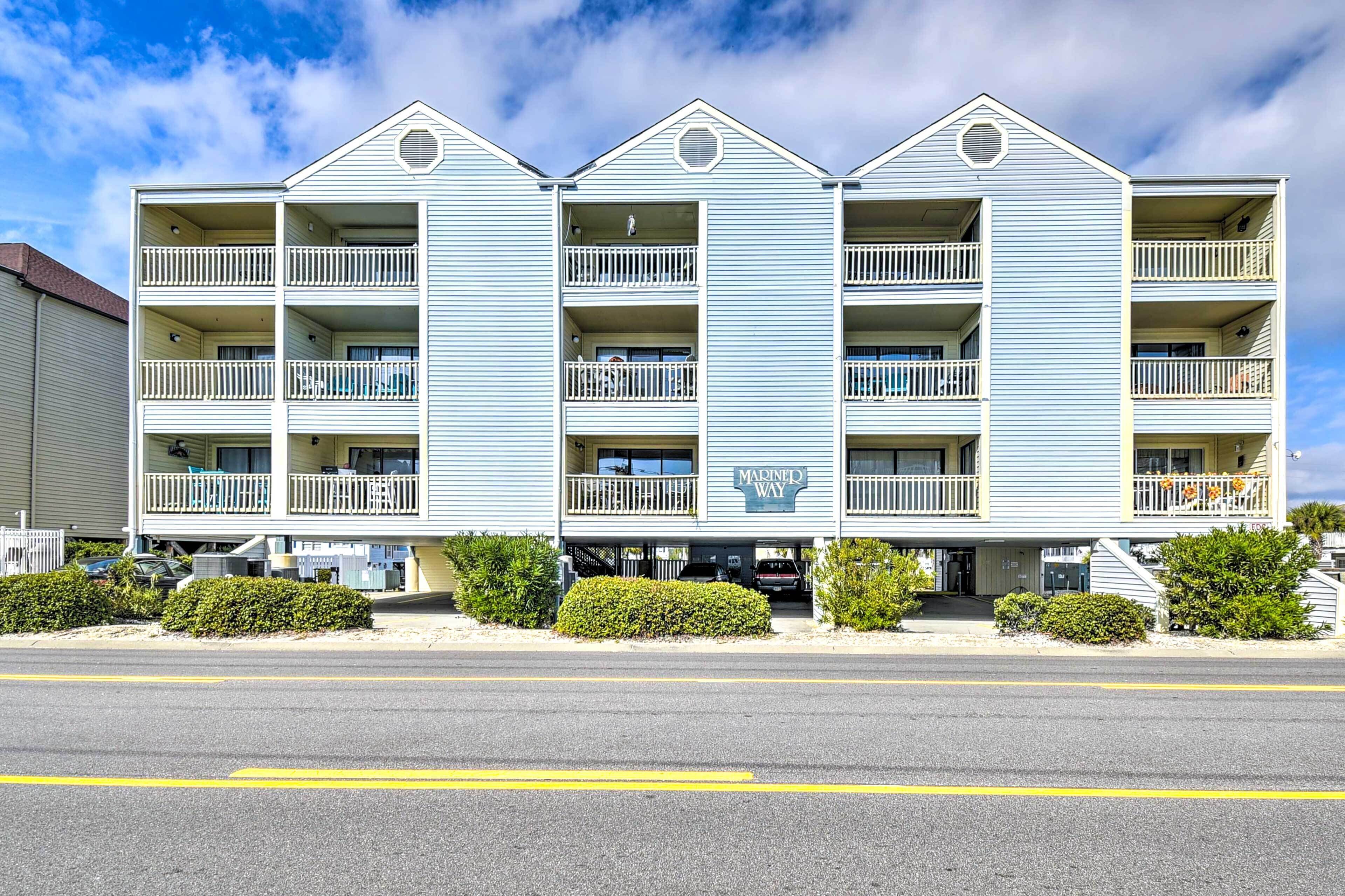 A multi-story hotel with balconies, a sign reading "Madin's Way," and a parking area in front.