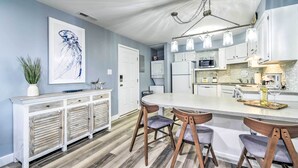 A modern kitchen with a central island, white cabinetry, and a hanging light fixture.