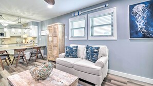 A modern kitchen with white cabinets, a dining area with a wooden table, and a gray sofa with nautical-themed pillows.