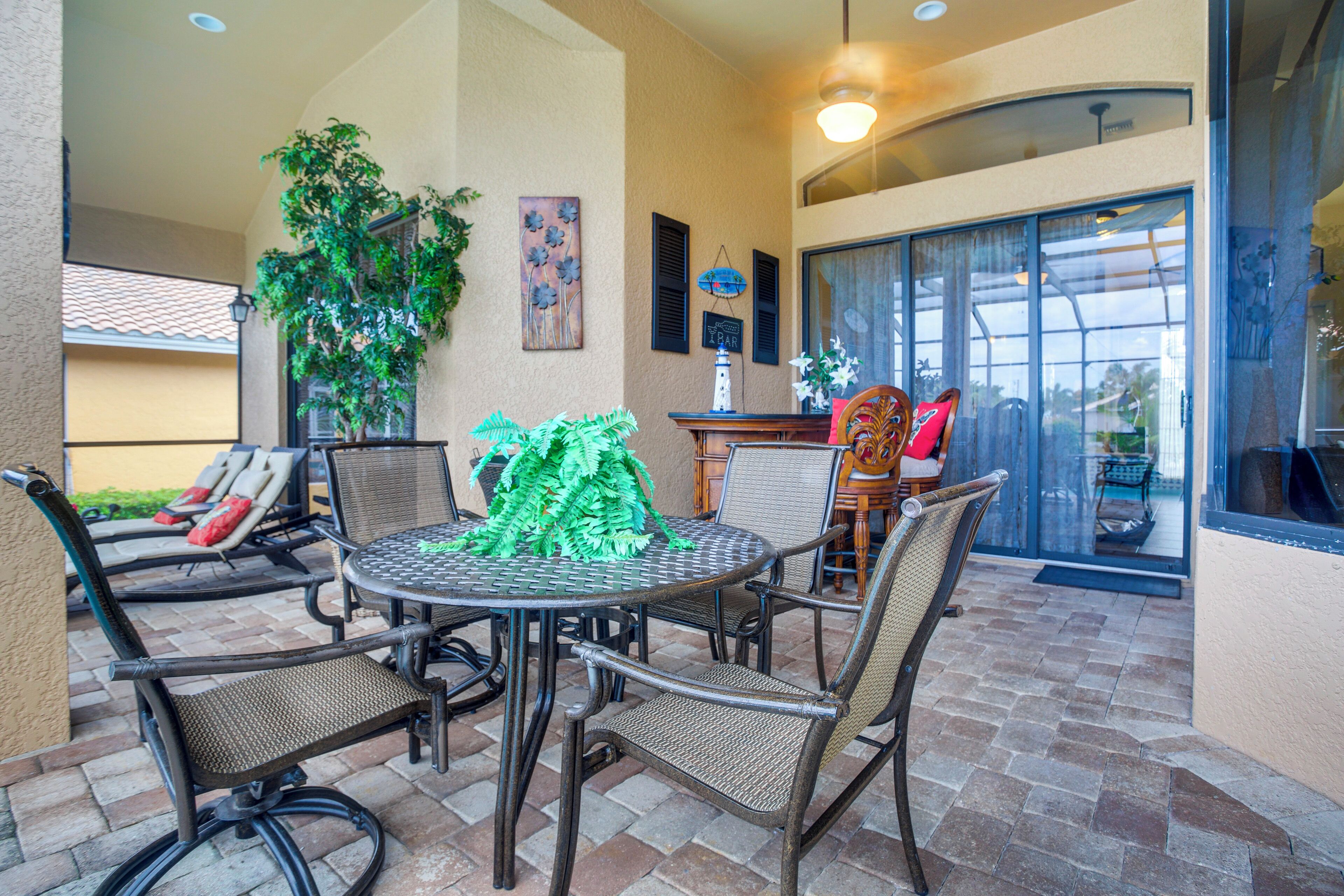 An outdoor patio with a round table, wicker chairs, a potted plant, and a view of the interior through a glass door.
