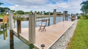 Une jetée en bois s’étendant sur une étendue d’eau calme, avec une chaise posée dessus, entourée de verdure et avec des immeubles résidentiels en arrière-plan.