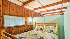 Een kamer met houten lambrisering, een bed, een raam met luiken en een lamp.