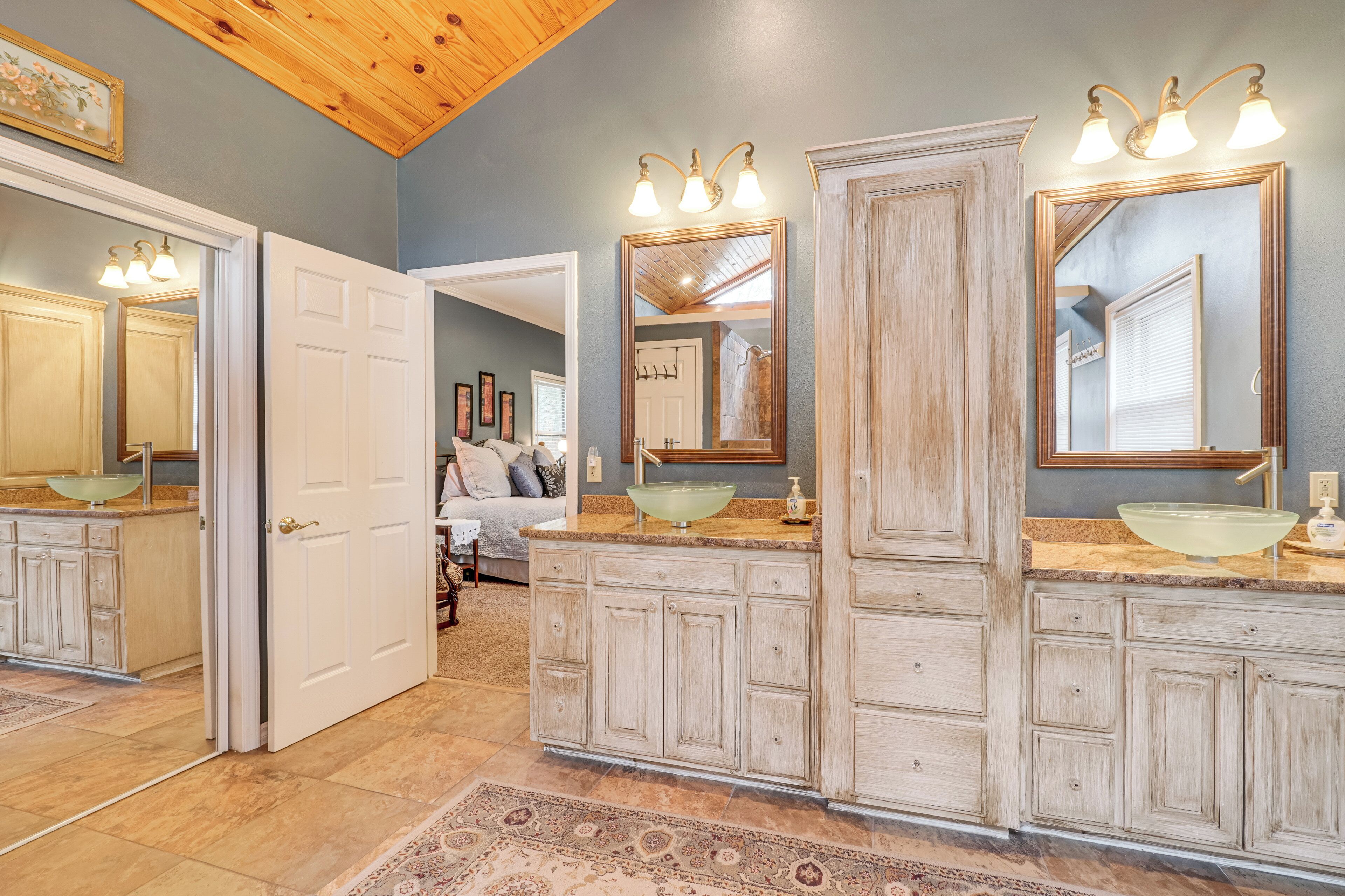 A bathroom with a large vanity, a glass bowl sink, and a mirror with lights.