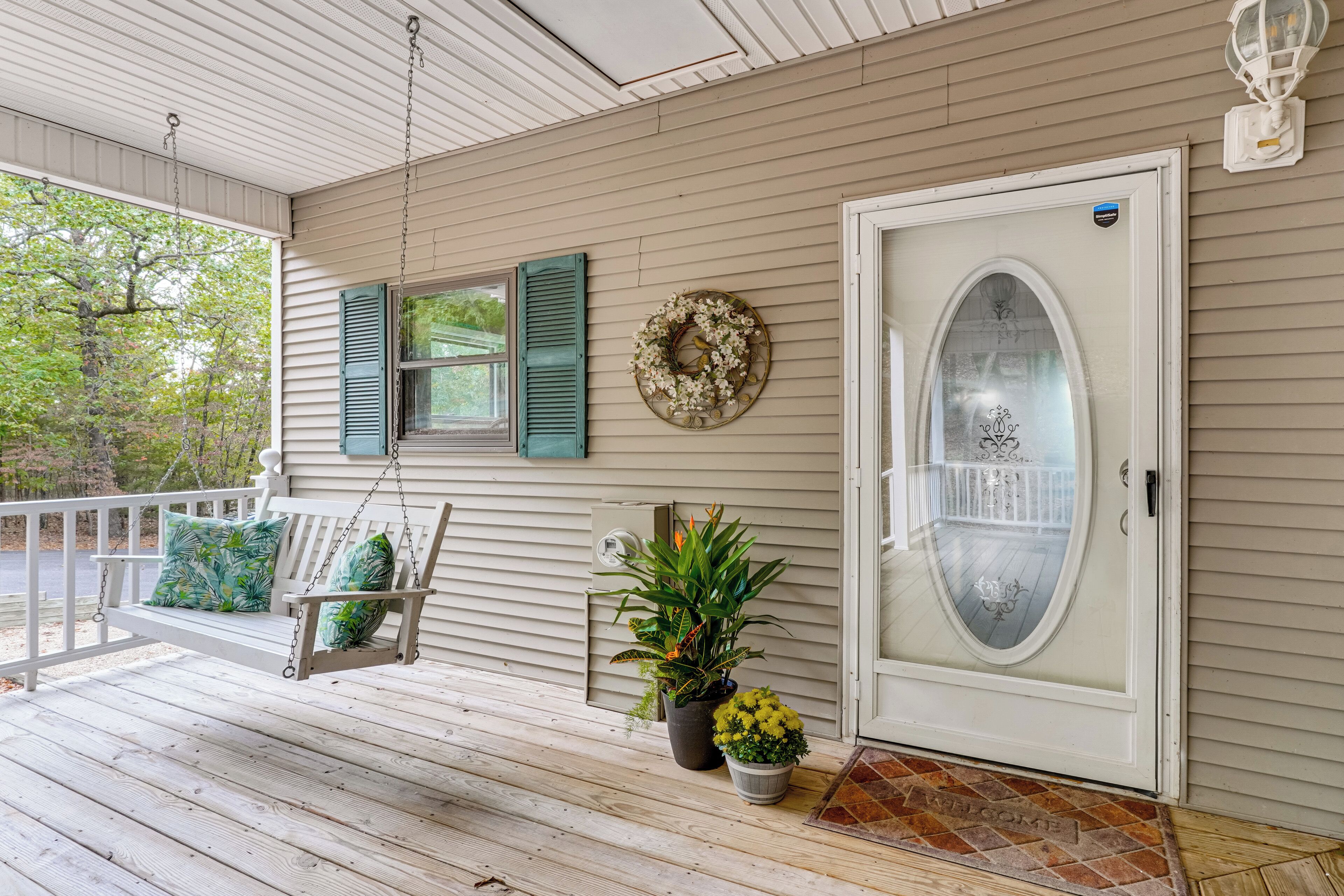 A porch with a swing, a door with a glass panel, and a wreath on the wall.