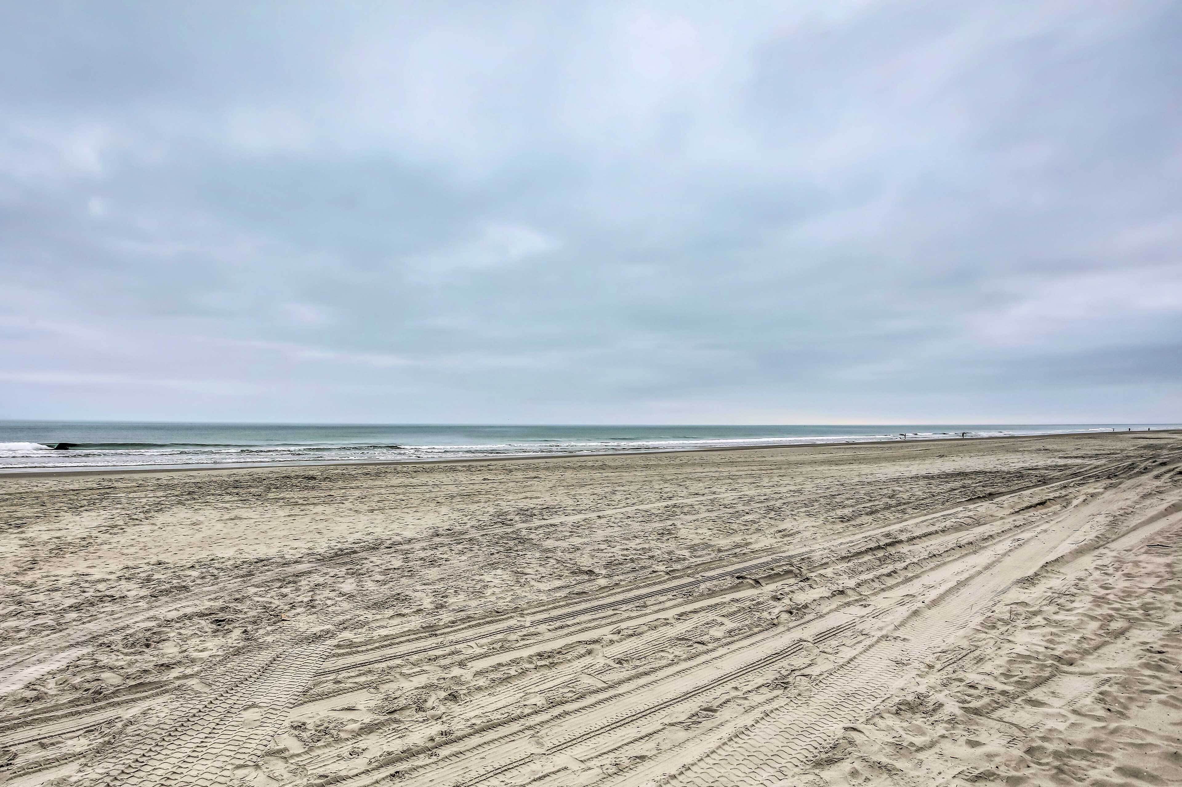 A wide sandy beach with tire tracks leading to the water.