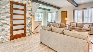 Un salon spacieux avec un grand canapé, une porte en bois dotée de panneaux en verre dépoli et un mur décoré d’un motif imitant la pierre.