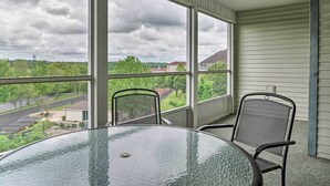 Ein Balkon mit Glastisch und zwei Stühlen, mit Blick auf einen Parkplatz und Grünflächen.